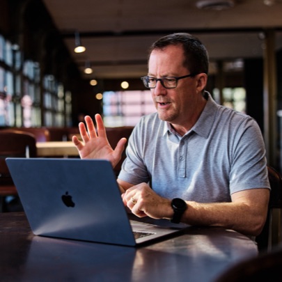 Photo of Greg Head on laptop waving to people on virtual meeting